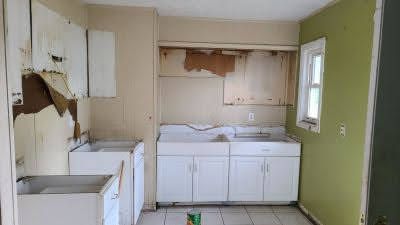 An empty kitchen with white cabinets , a sink , and a window.