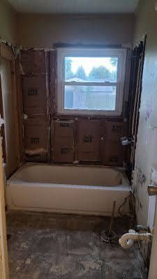 A bathroom with a tub and a window being remodeled.