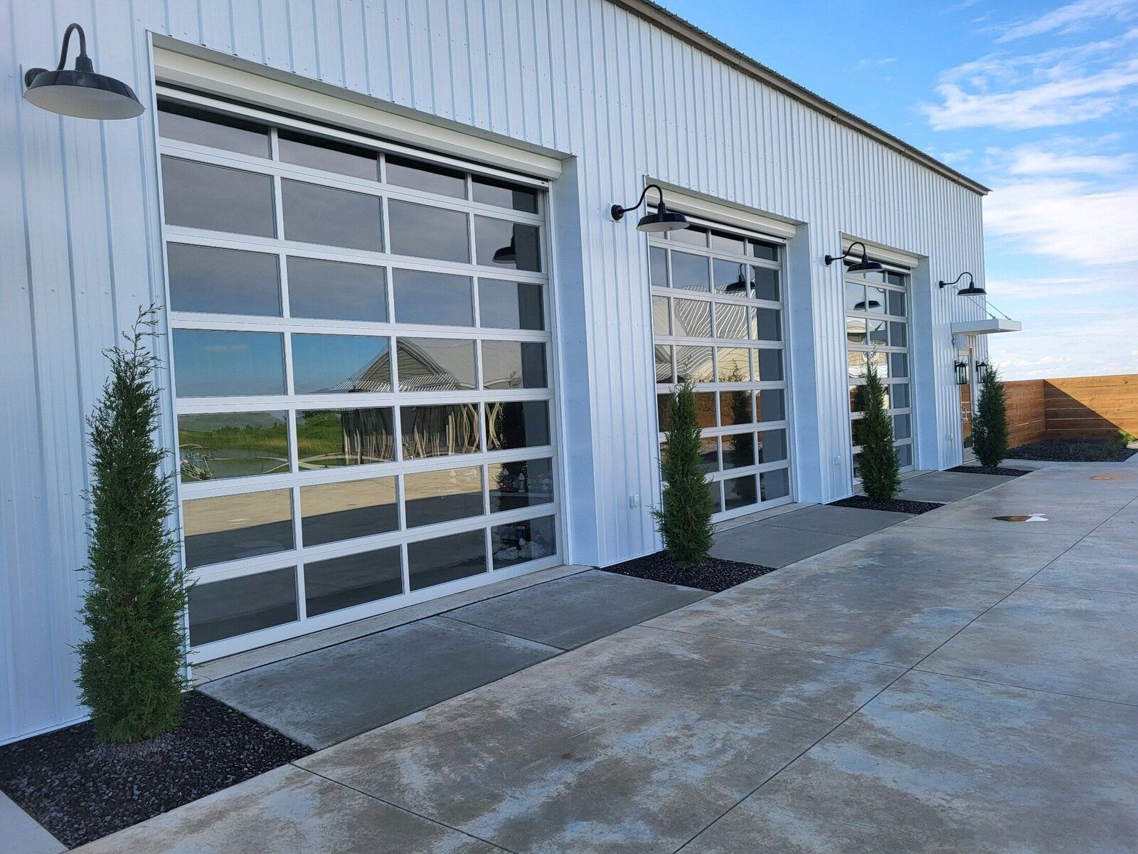 A row of garage doors on a white building with trees in front of them.