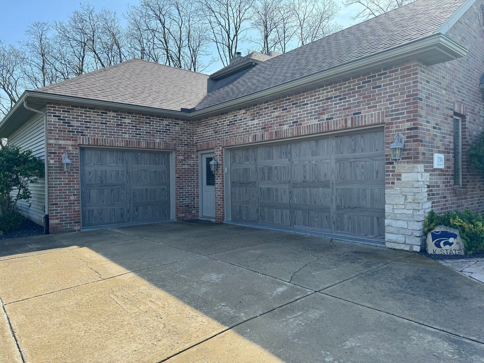 A brick house with two garage doors and a sign in front of it.