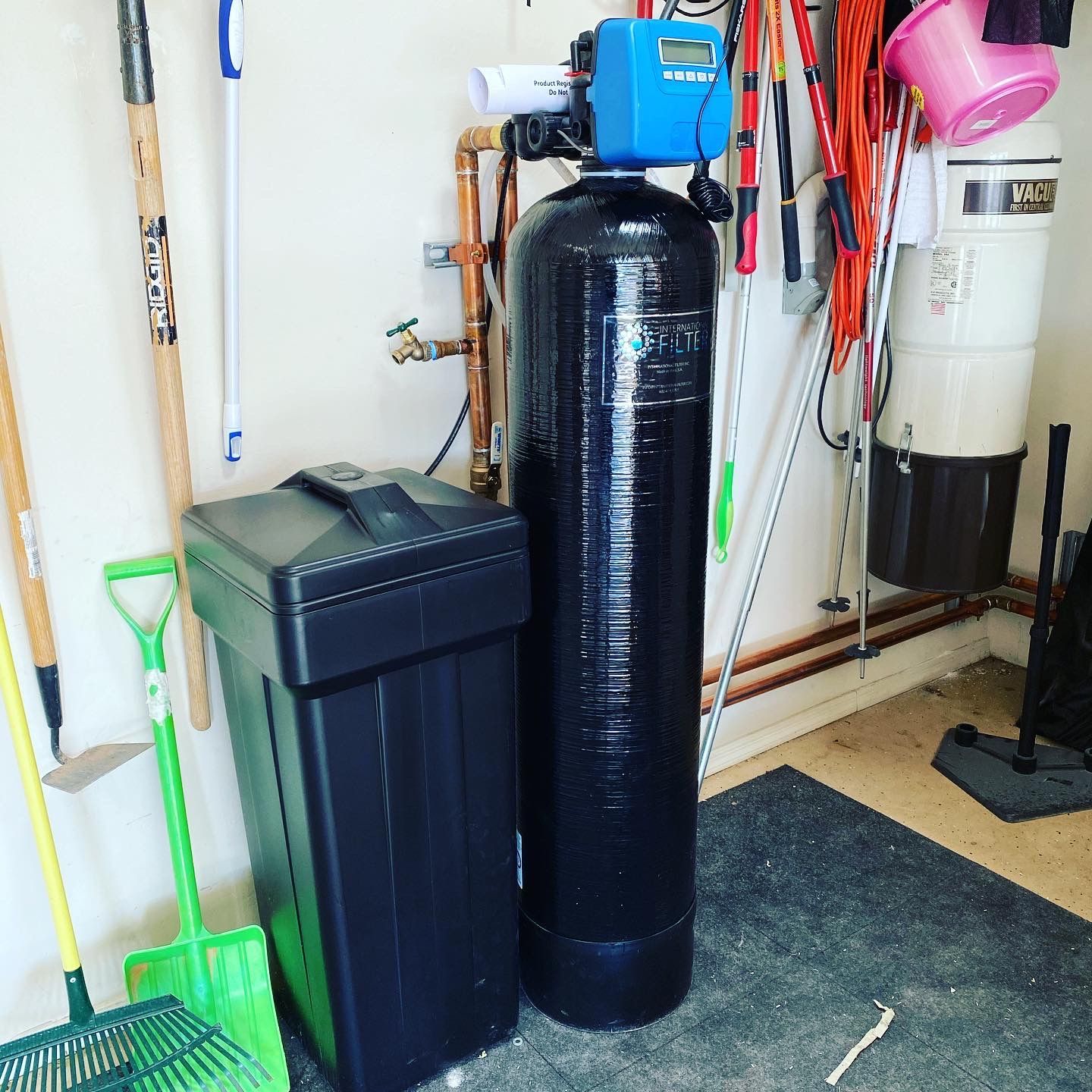 A black water filter is sitting next to a green trash can in a garage.