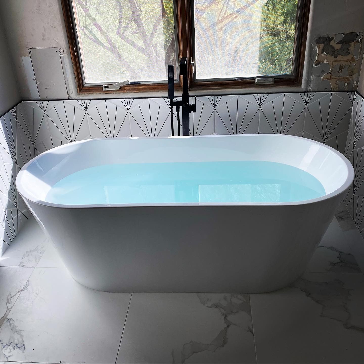 A bathtub filled with blue water in a bathroom next to a window.