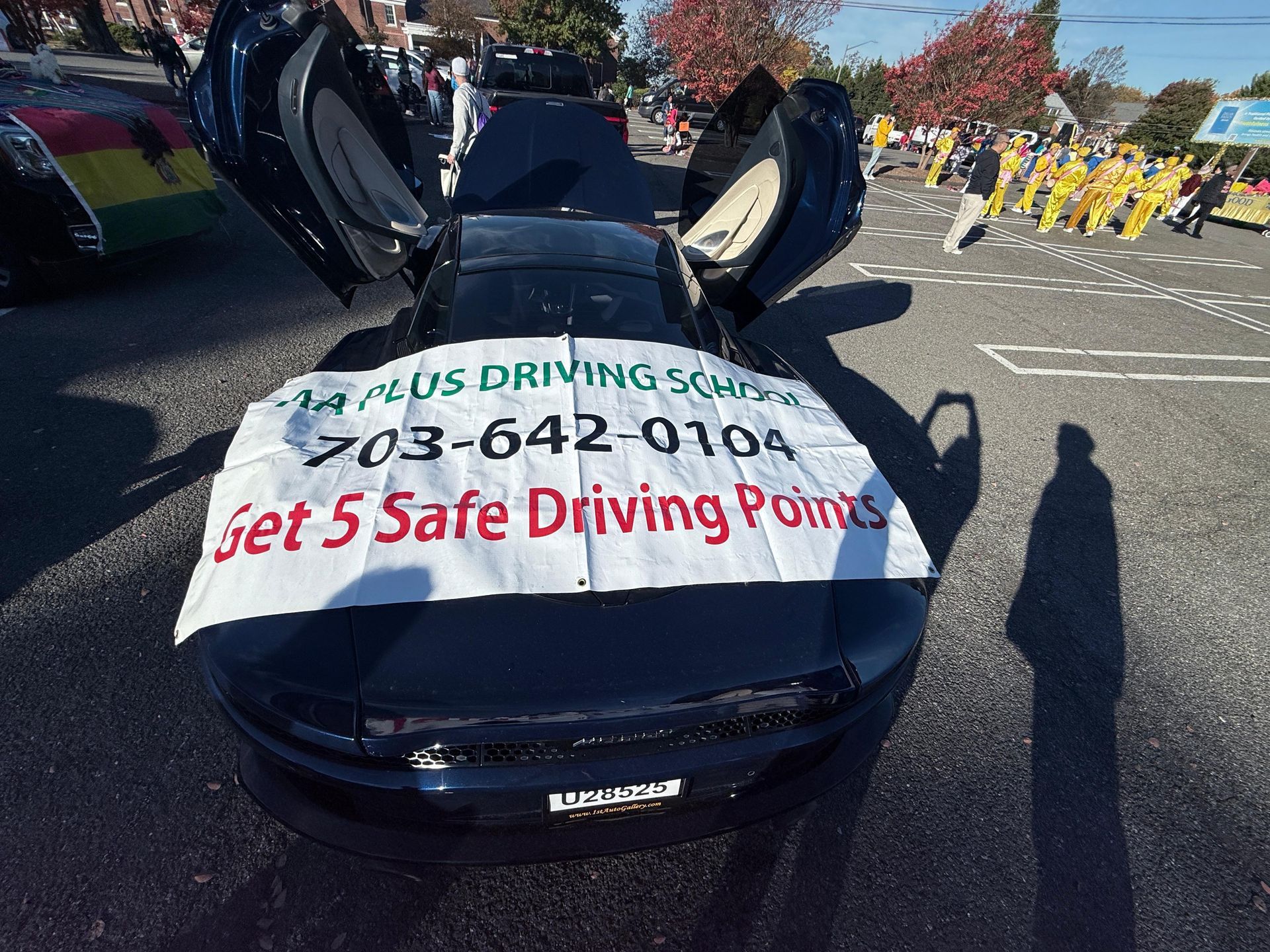 Black car with open doors displays a banner for a driving school, phone number, and