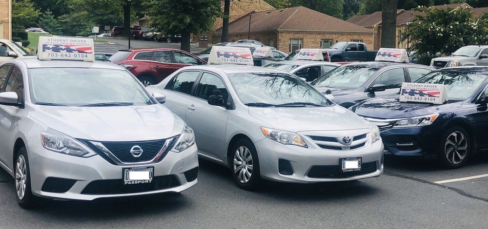 Silver sedans parked in a lot with signs on their roofs, likely for a driving school or service.