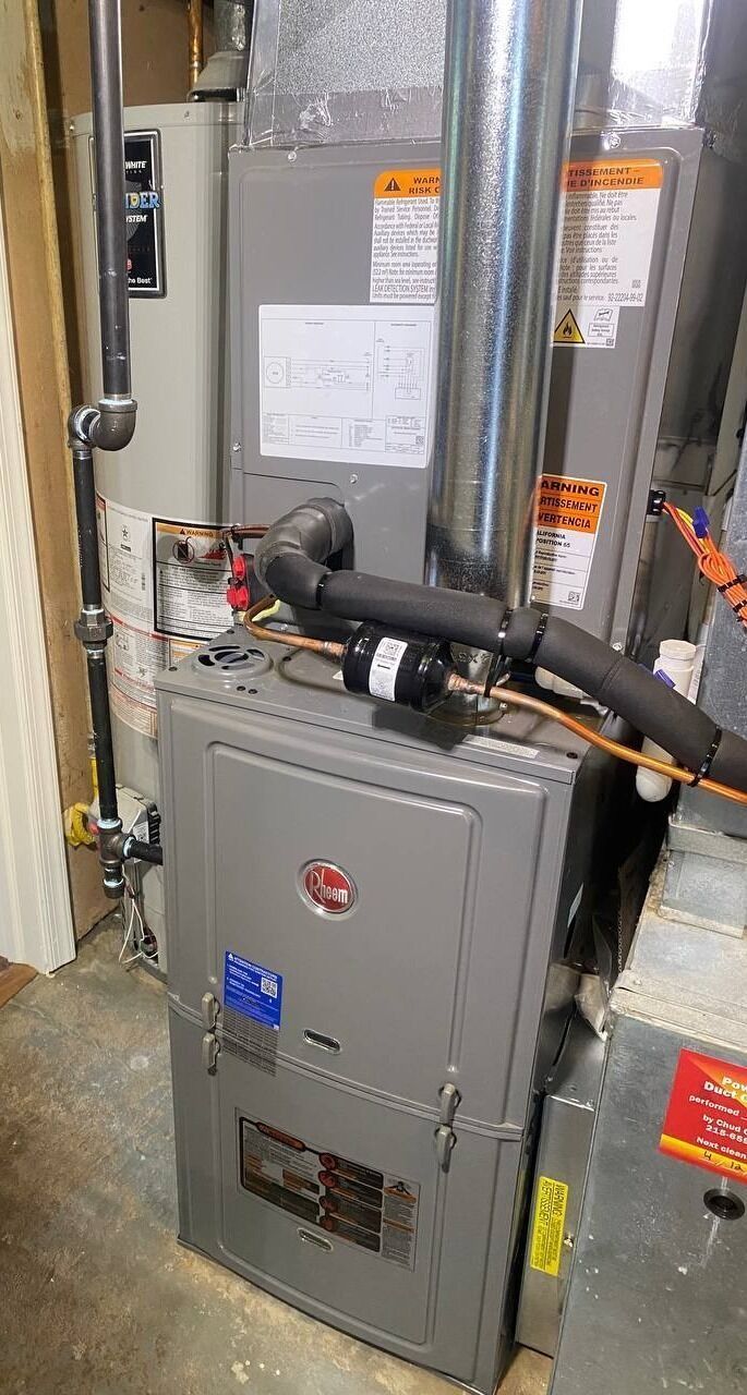 A furnace and water heater in a utility room. Gray metal units with pipes and ductwork.