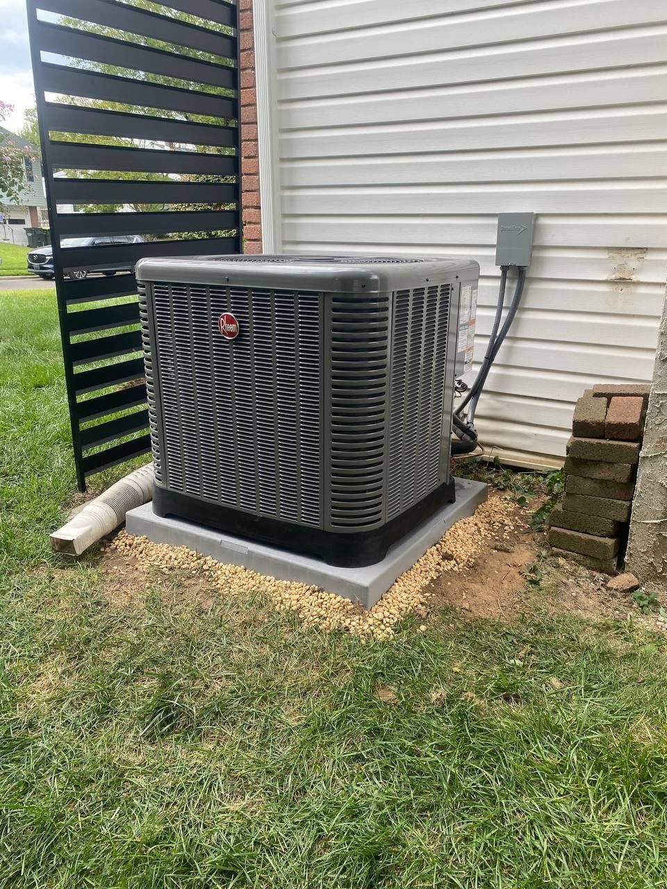 Gray Rheem air conditioner unit on concrete pad next to a house and black privacy screen.