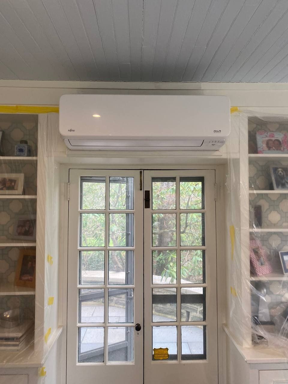 White air conditioning unit above glass double doors, flanked by built-in shelves.