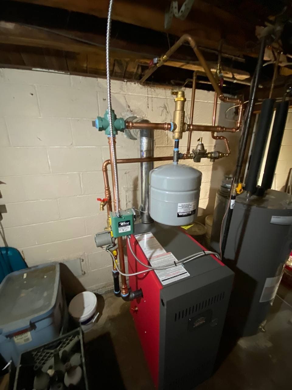 Heating system in a basement with red boiler, copper pipes, and expansion tank.