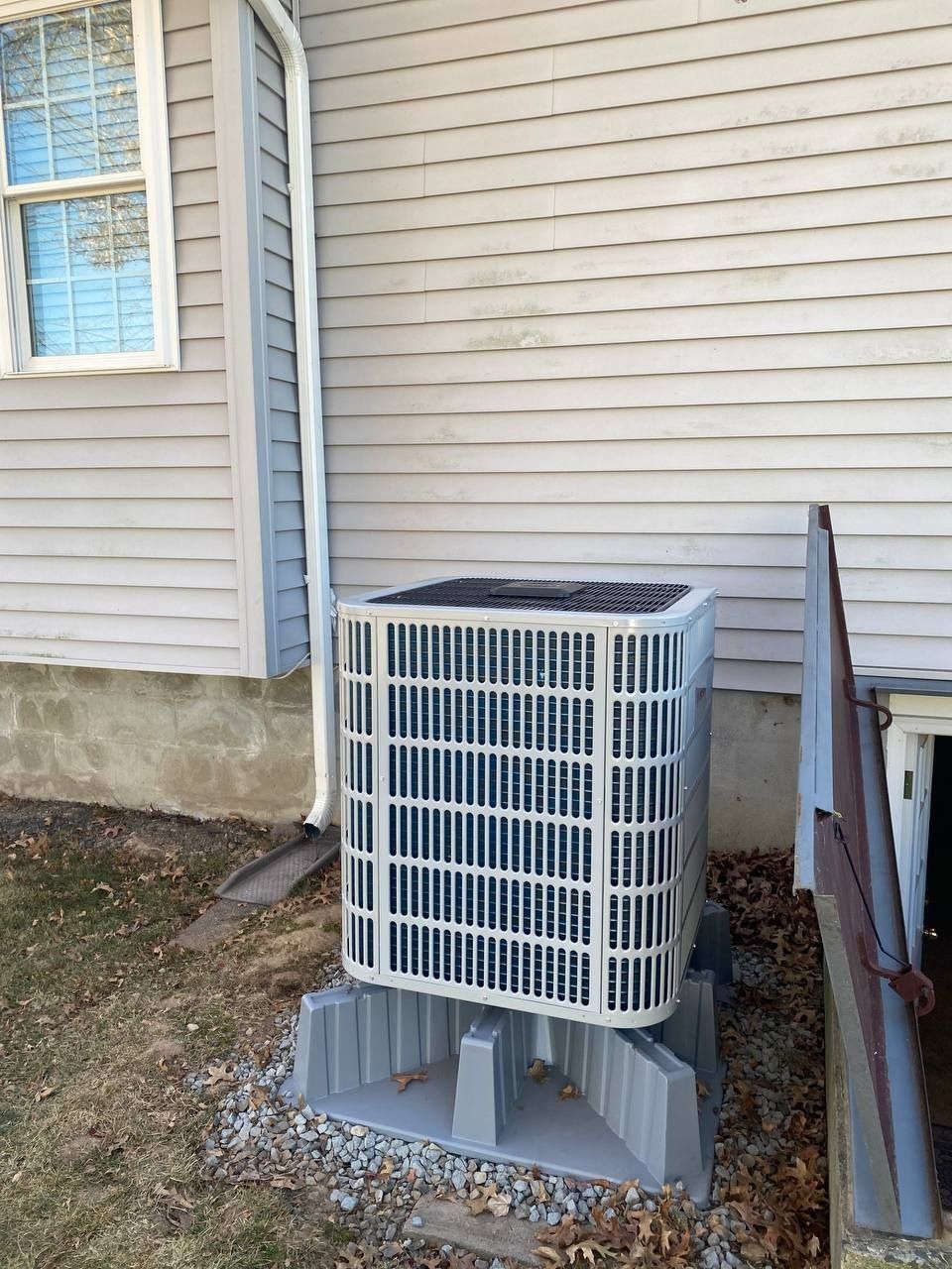 Air conditioning unit outdoors, on concrete blocks, next to a building with siding.