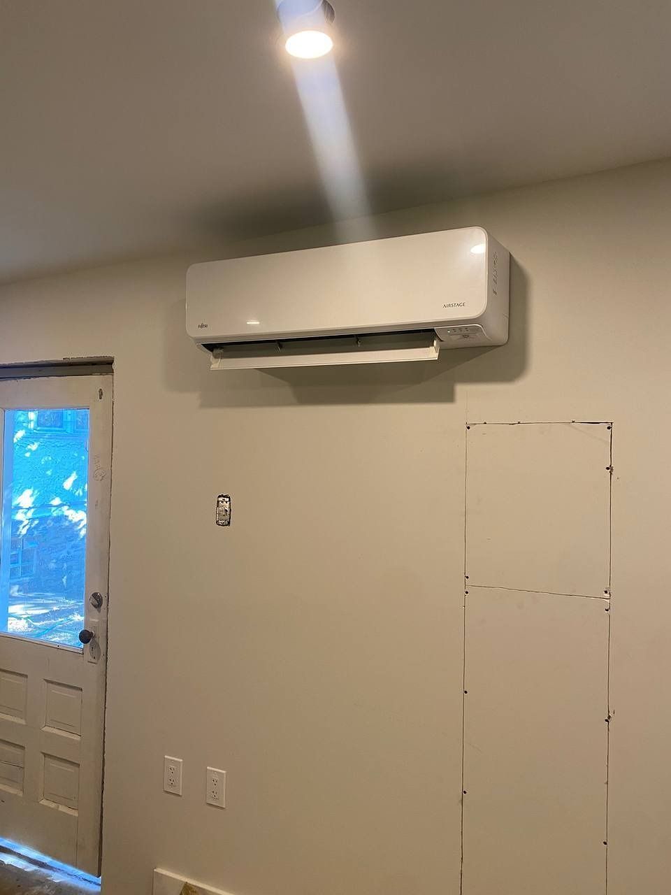 White air conditioner unit mounted on a beige wall above a door.