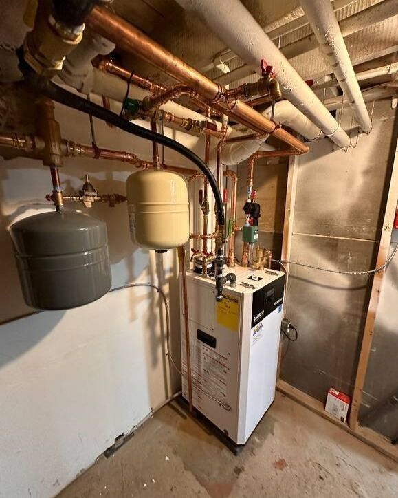 A boiler system with copper pipes, expansion tanks, and insulation in a utility room.