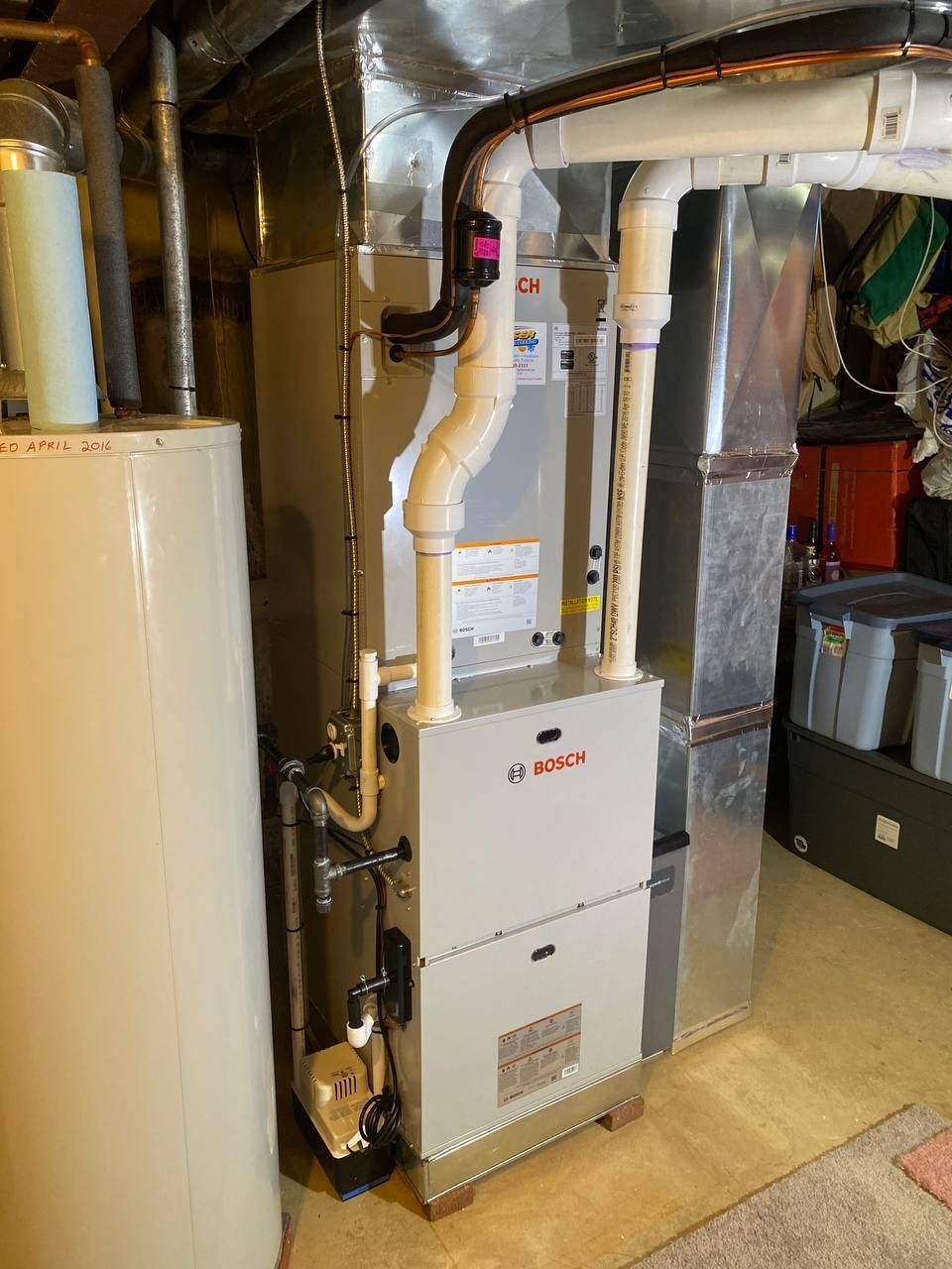 Furnace and water heater in a basement. The furnace is white and silver with white vent pipes.