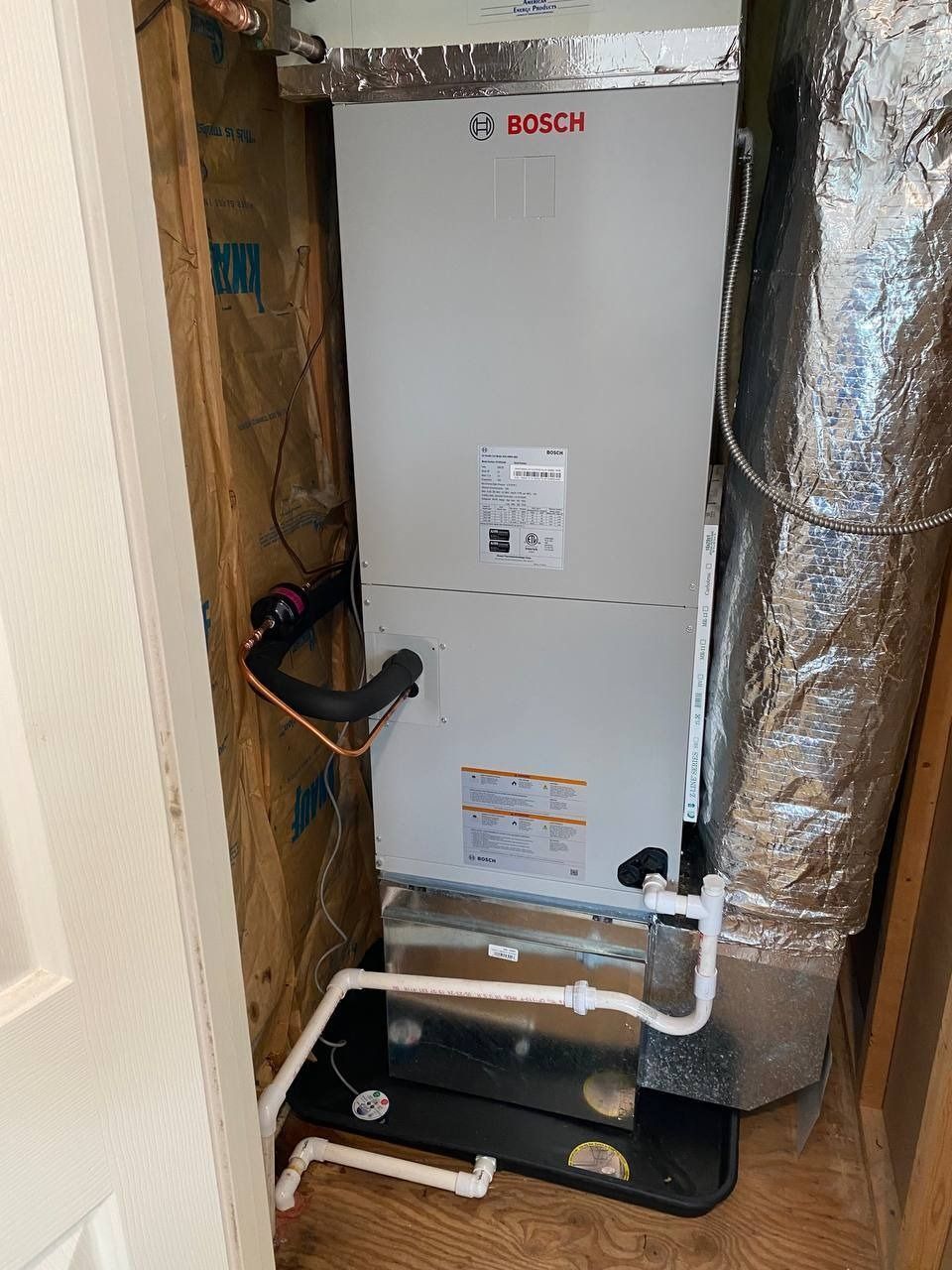 Bosch HVAC unit in a utility closet with ductwork and PVC pipes.