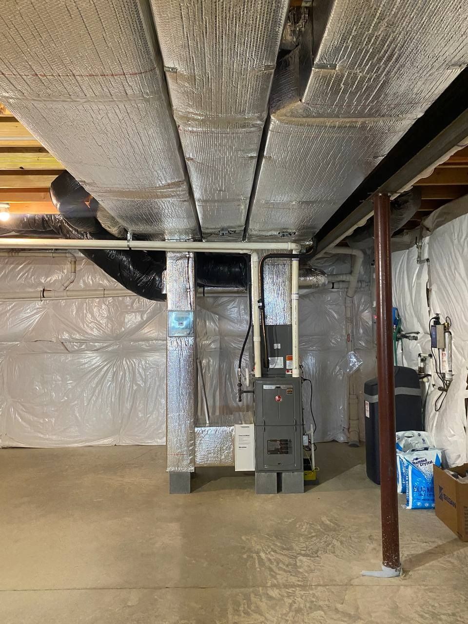 Basement with ductwork covered in insulation, electrical panel, and support beams.