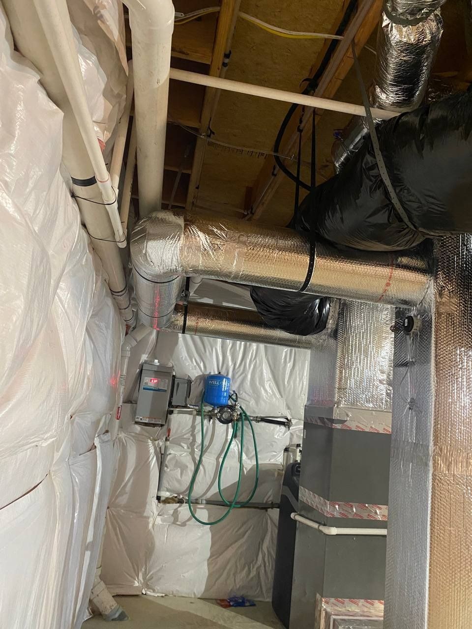 Basement interior with water pipes, insulation, ductwork, and equipment. White, silver, and black materials.