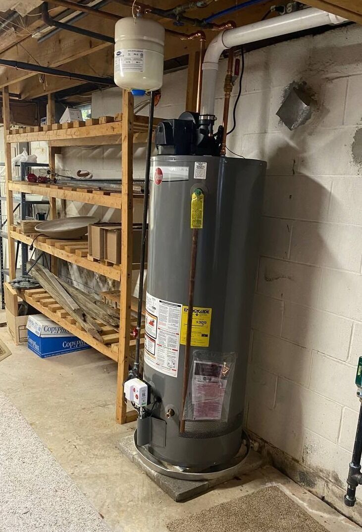 A tall, gray water heater with copper piping, a white expansion tank, and a wooden shelf in a basement.