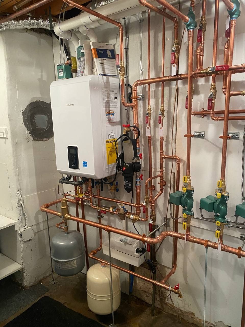 Copper pipes and boiler on a basement wall. Several valves, gauges, and tanks are visible.