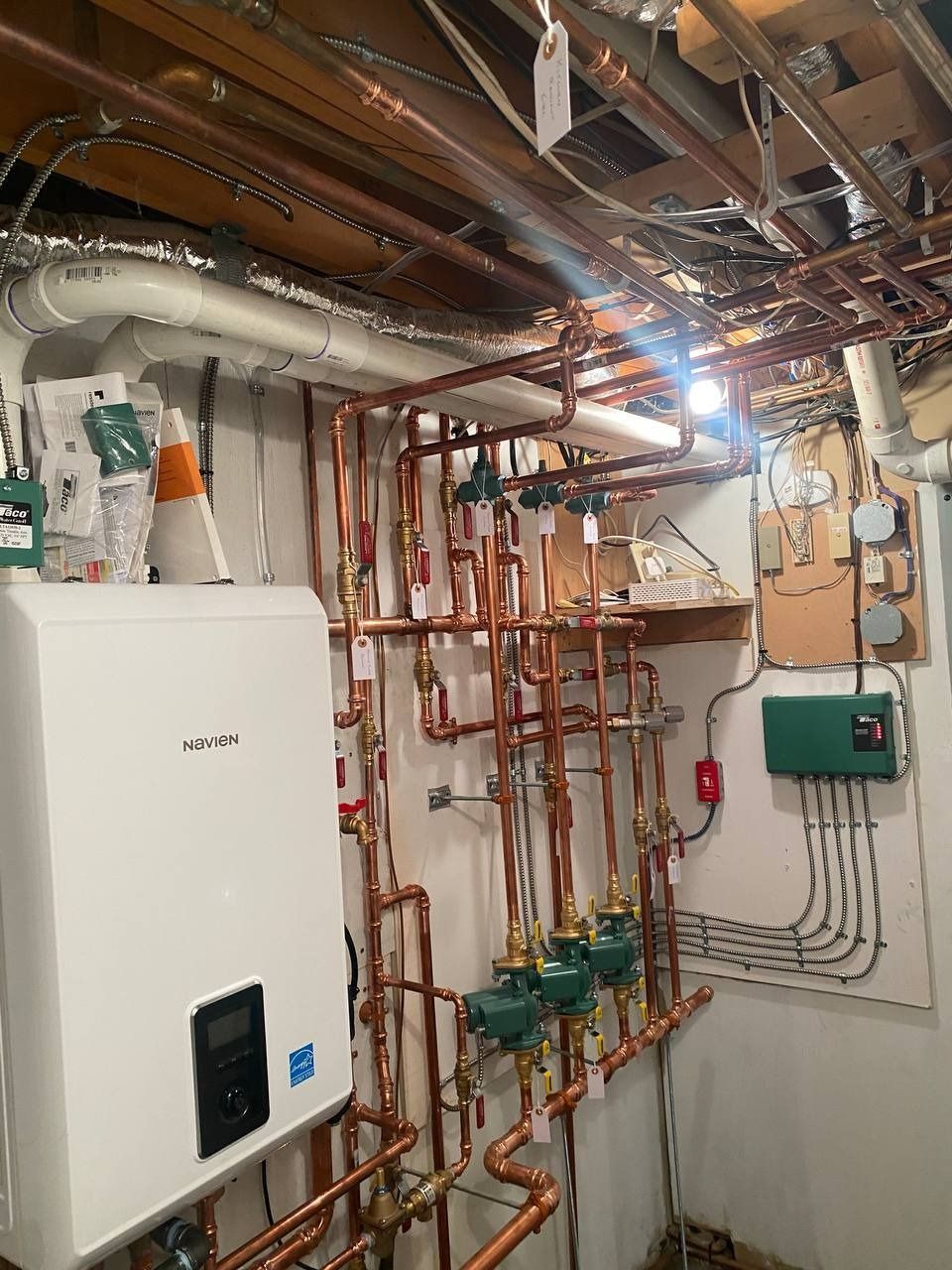 White wall-mounted boiler and complex copper piping system in a basement.