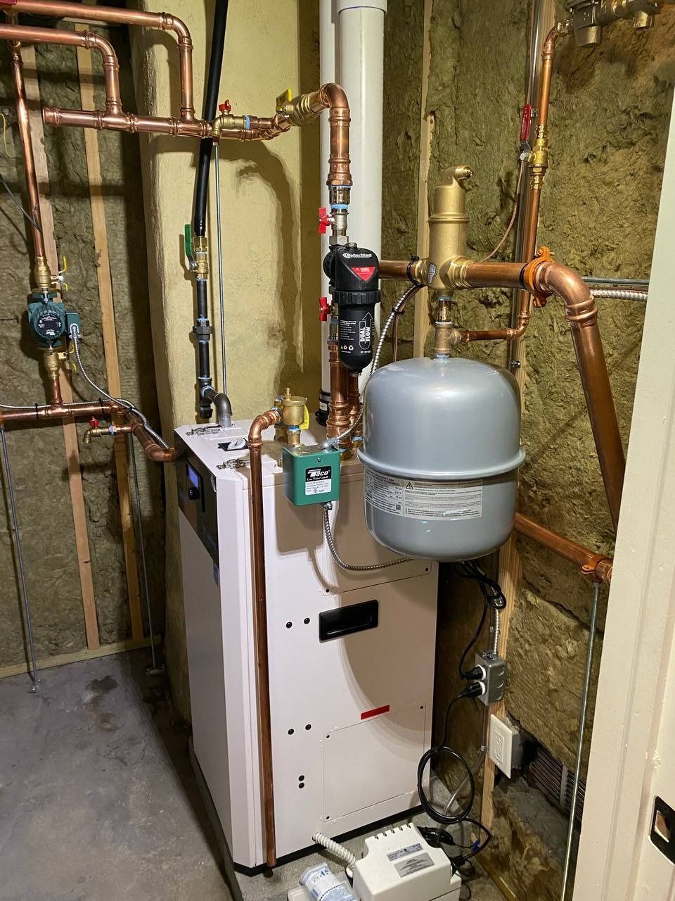 A boiler system with copper pipes, a gray expansion tank, and various valves, installed in a basement.