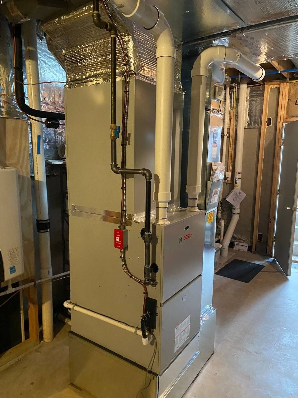 Furnace and ductwork in a basement. Metal cabinet, pipes, and vents. Silver, black, and white.