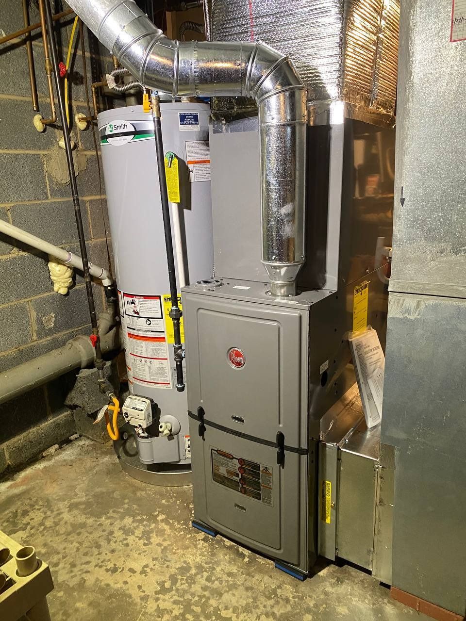 A furnace and water heater in a basement. The furnace has a silver duct leading to the ceiling.