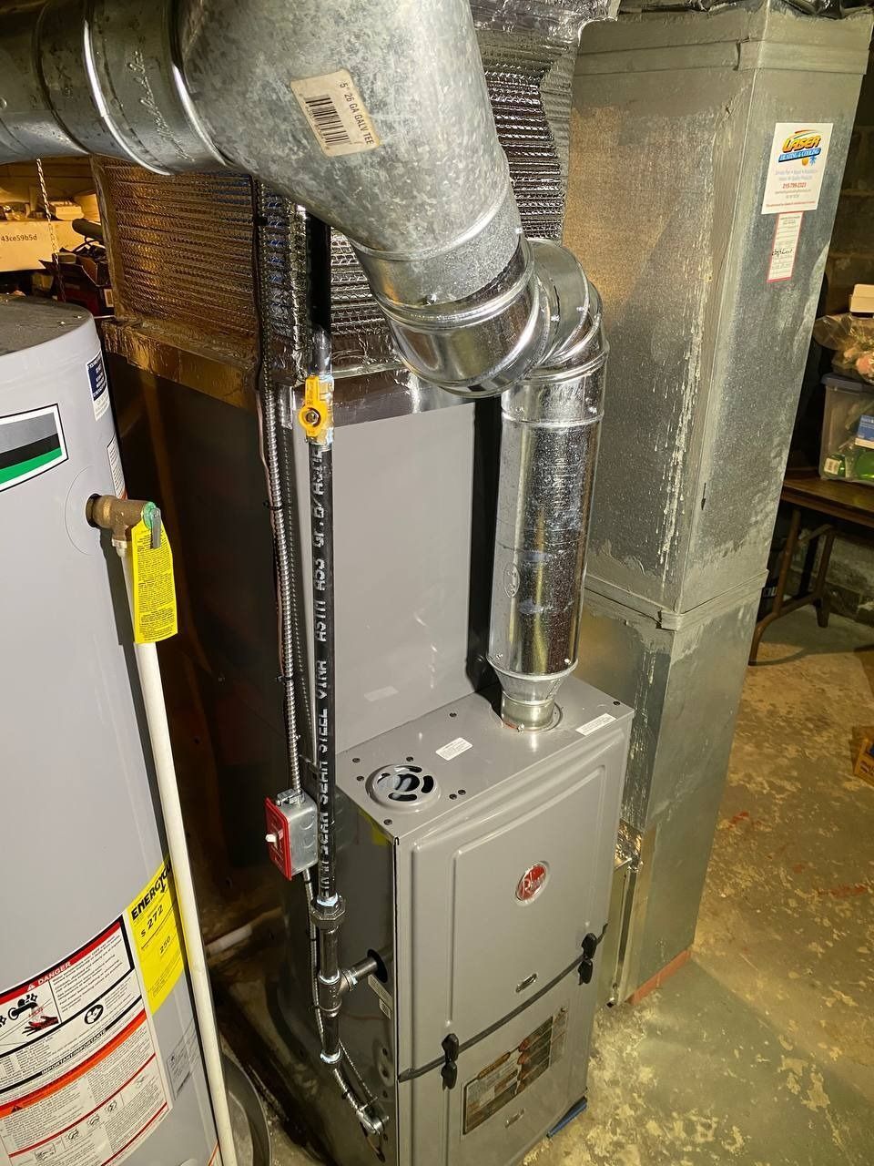 Furnace with ductwork and water heater in a basement. Grey metal appliances.