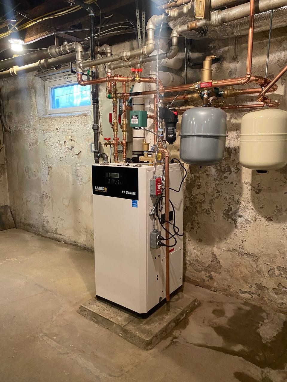 White furnace in a basement with copper pipes and two expansion tanks.
