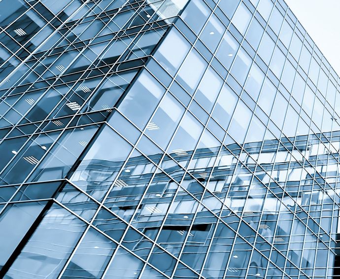 Glass facade of a modern building reflecting surrounding structures, blue-toned.