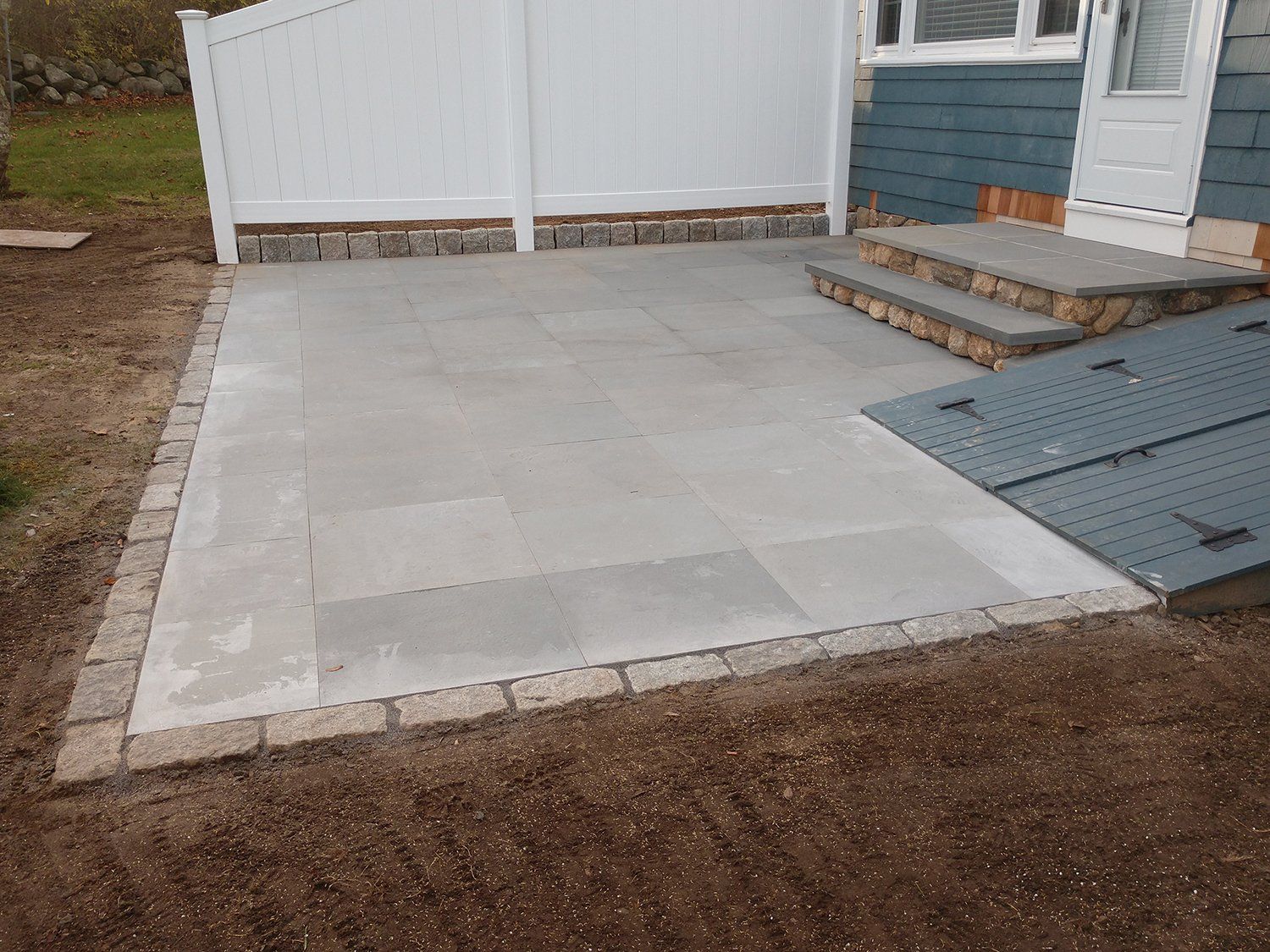 A patio with steps and a white fence in front of a house