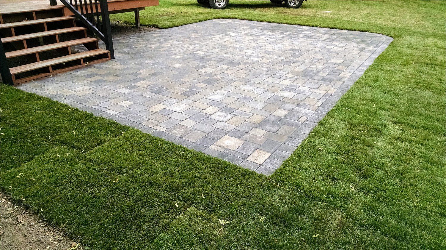 A car is parked in the grass next to a brick patio