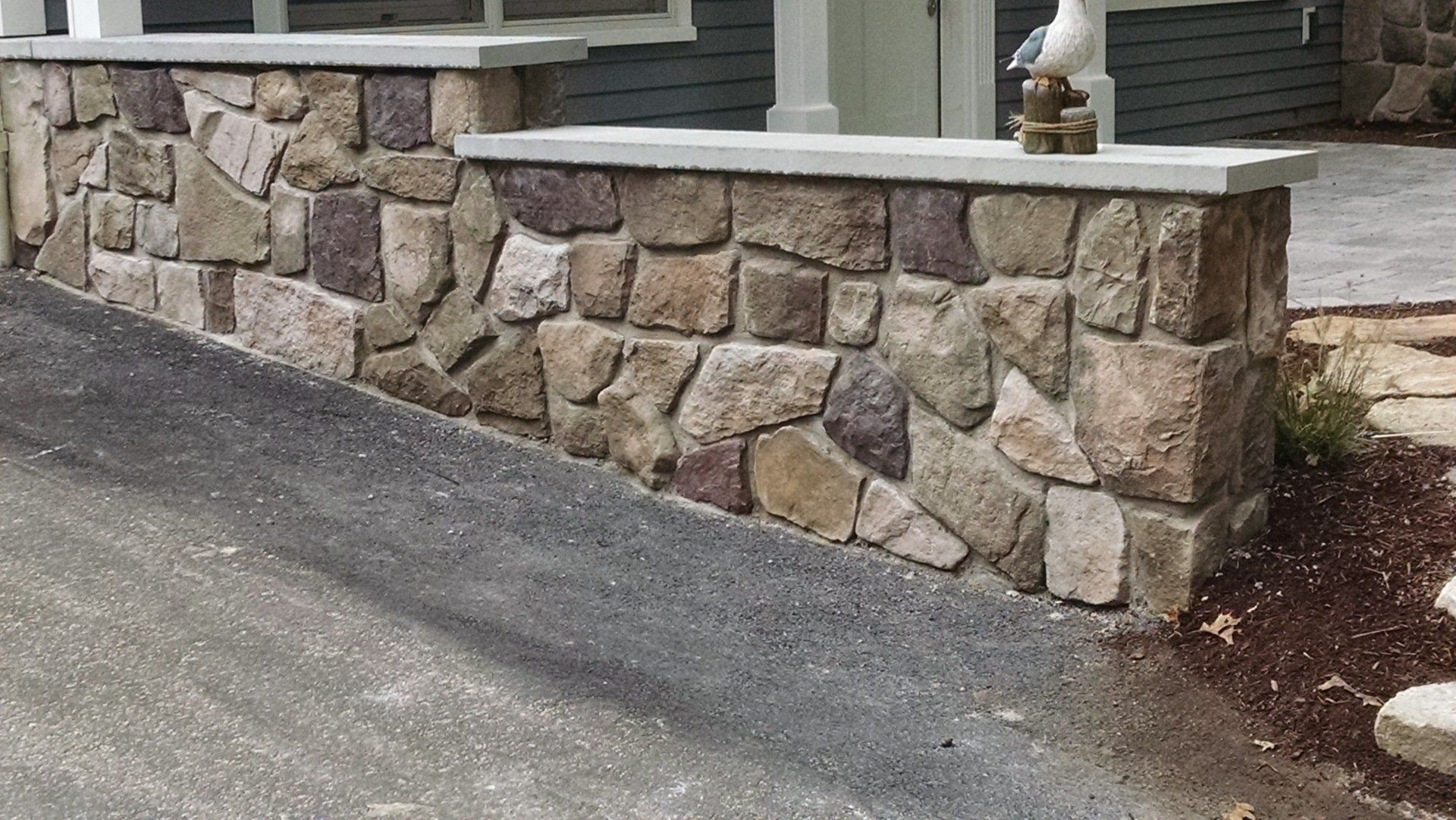 A stone wall along the side of a road next to a house.