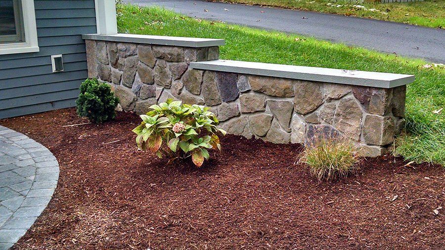 A stone wall with two benches in front of a house.