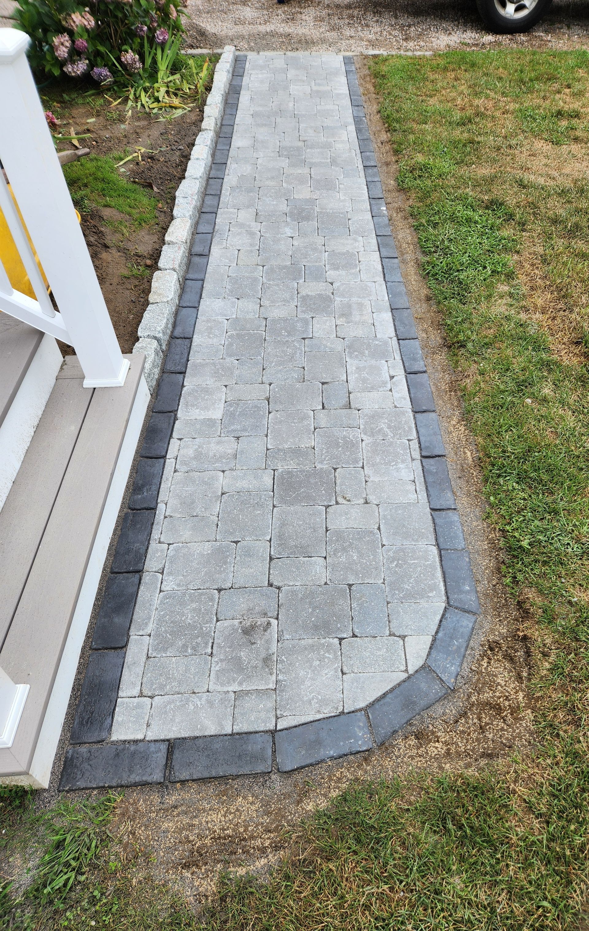 A brick walkway leading to a house with a car parked on the side of it.