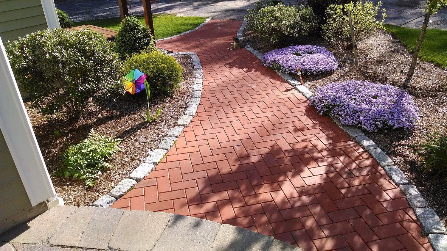 A red brick walkway with purple flowers and a windmill in the middle