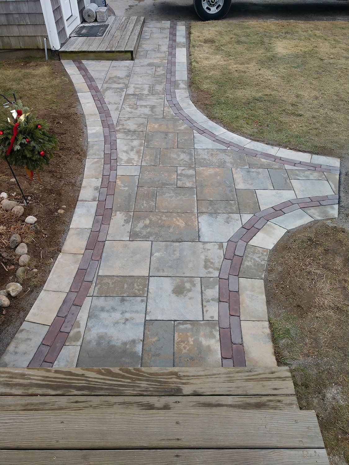 A stone walkway leading to a house with a car parked in the background.