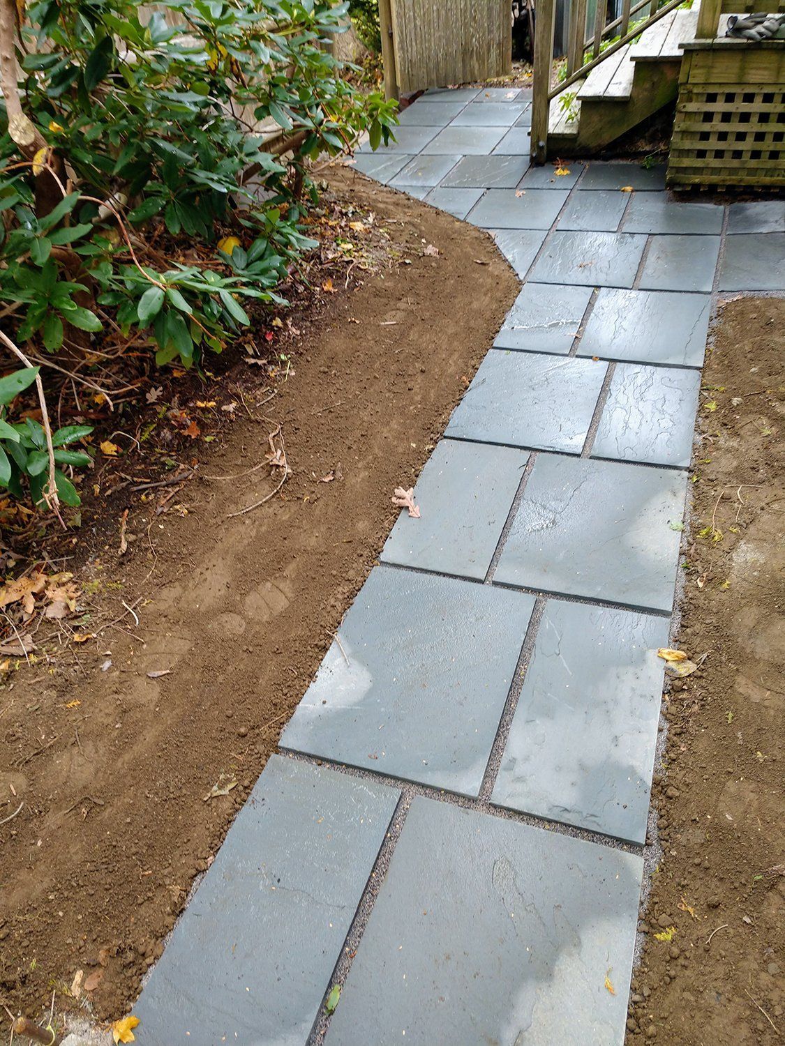 A stone walkway leading to a deck in a backyard.