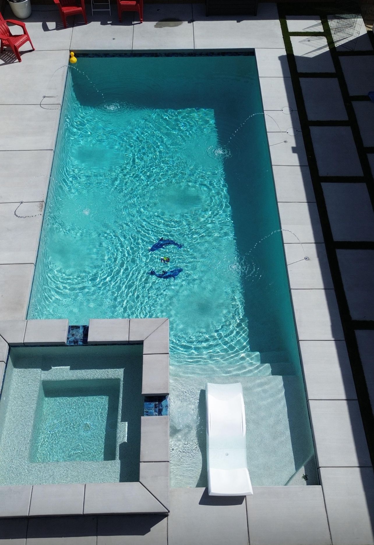 Aerial view of a turquoise swimming pool beside a hot tub and white deck chairs