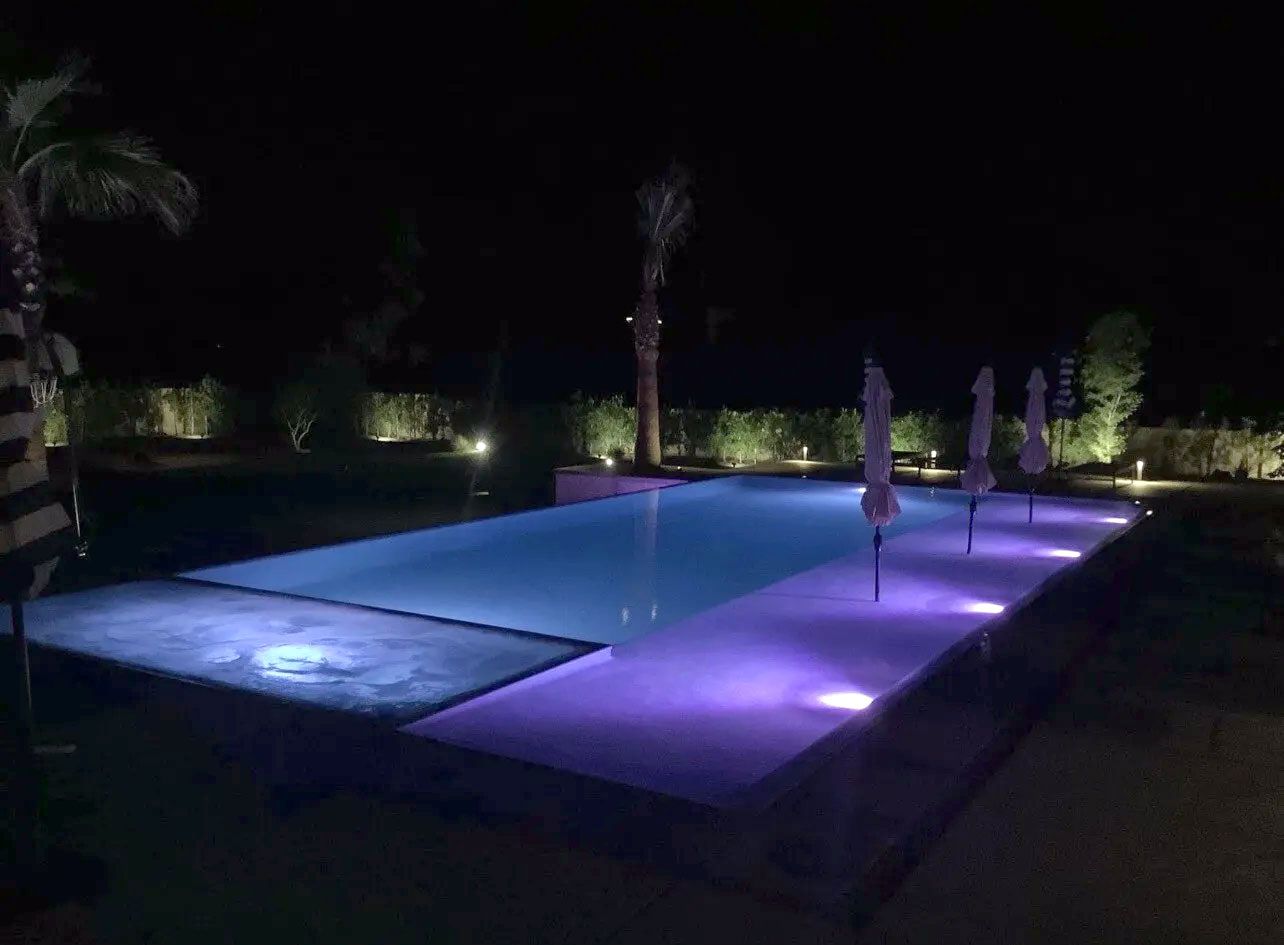 A large swimming pool is lit up at night with purple lights.