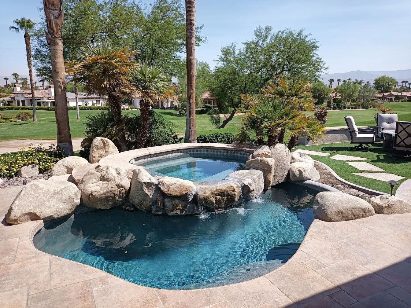A large swimming pool surrounded by rocks and trees in a backyard.