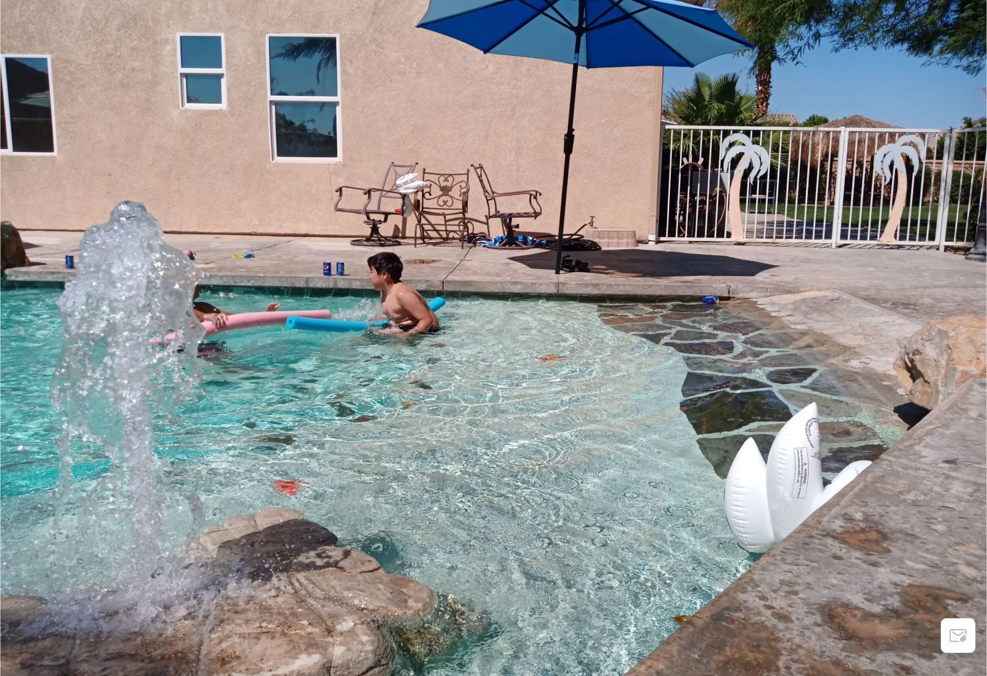 Two children are playing in a swimming pool under an umbrella