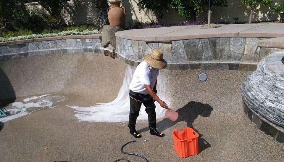 A man wearing a hat is cleaning a swimming pool