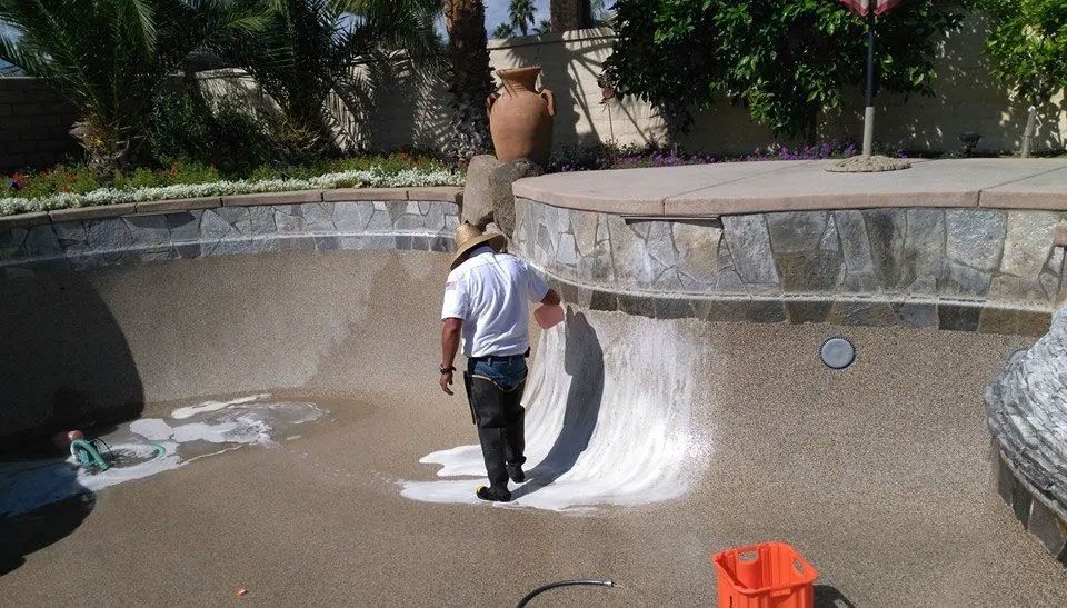 A man is painting a pool with a vacuum cleaner.