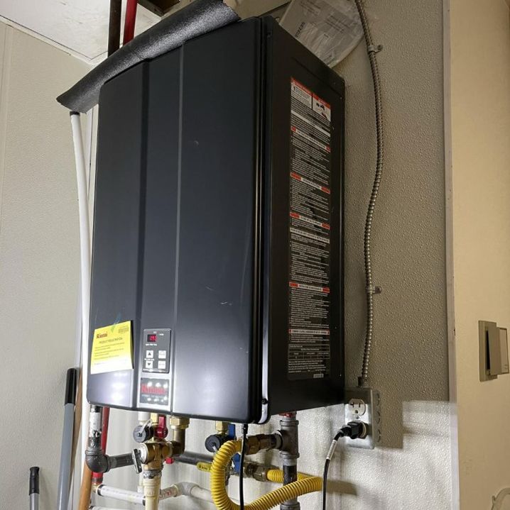 Black tankless water heater mounted on a wall with pipes and controls.