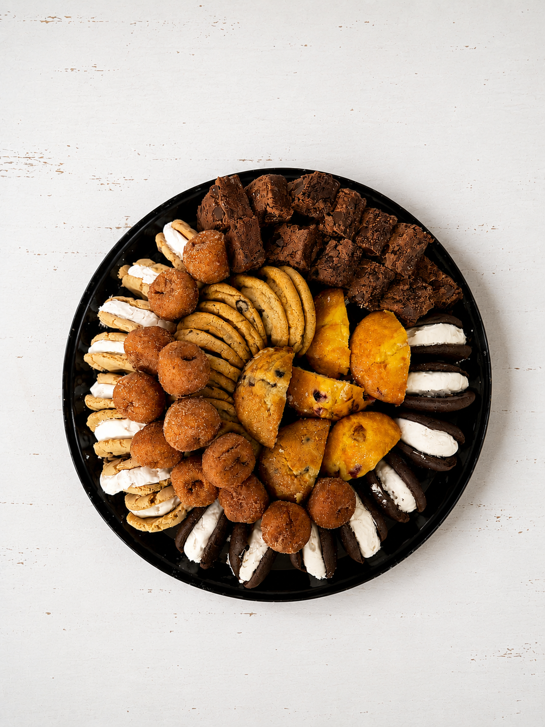 Assorted cookies and pastries arranged in a circular black tray on a white background