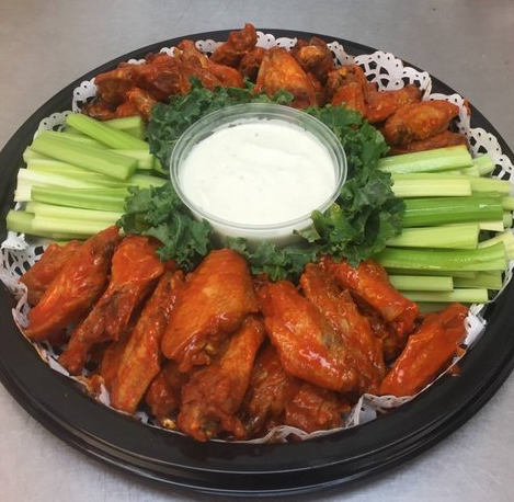 Buffalo wings arranged on a platter with celery sticks and a central cup of white dipping sauce