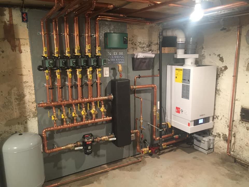 A boiler is sitting in a basement next to a wall with copper pipes.