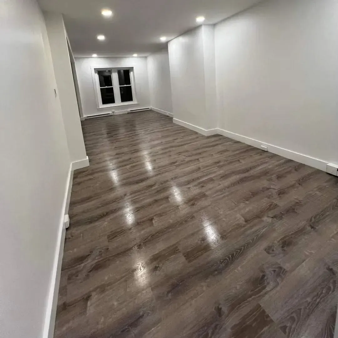 Empty room with wood-look flooring and white walls. A window is in the background.