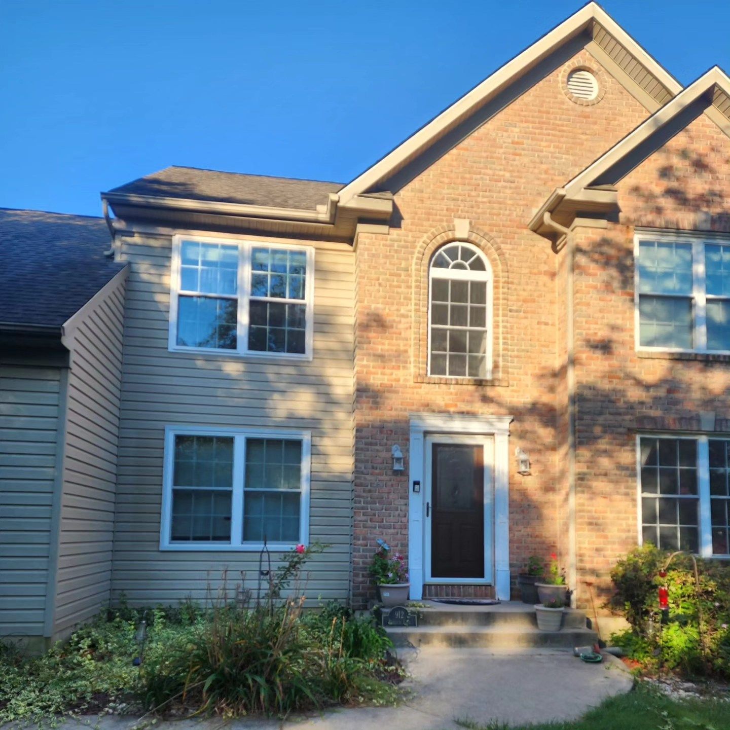 Two-story house with brick facade, beige siding, windows, and a front door with small steps.