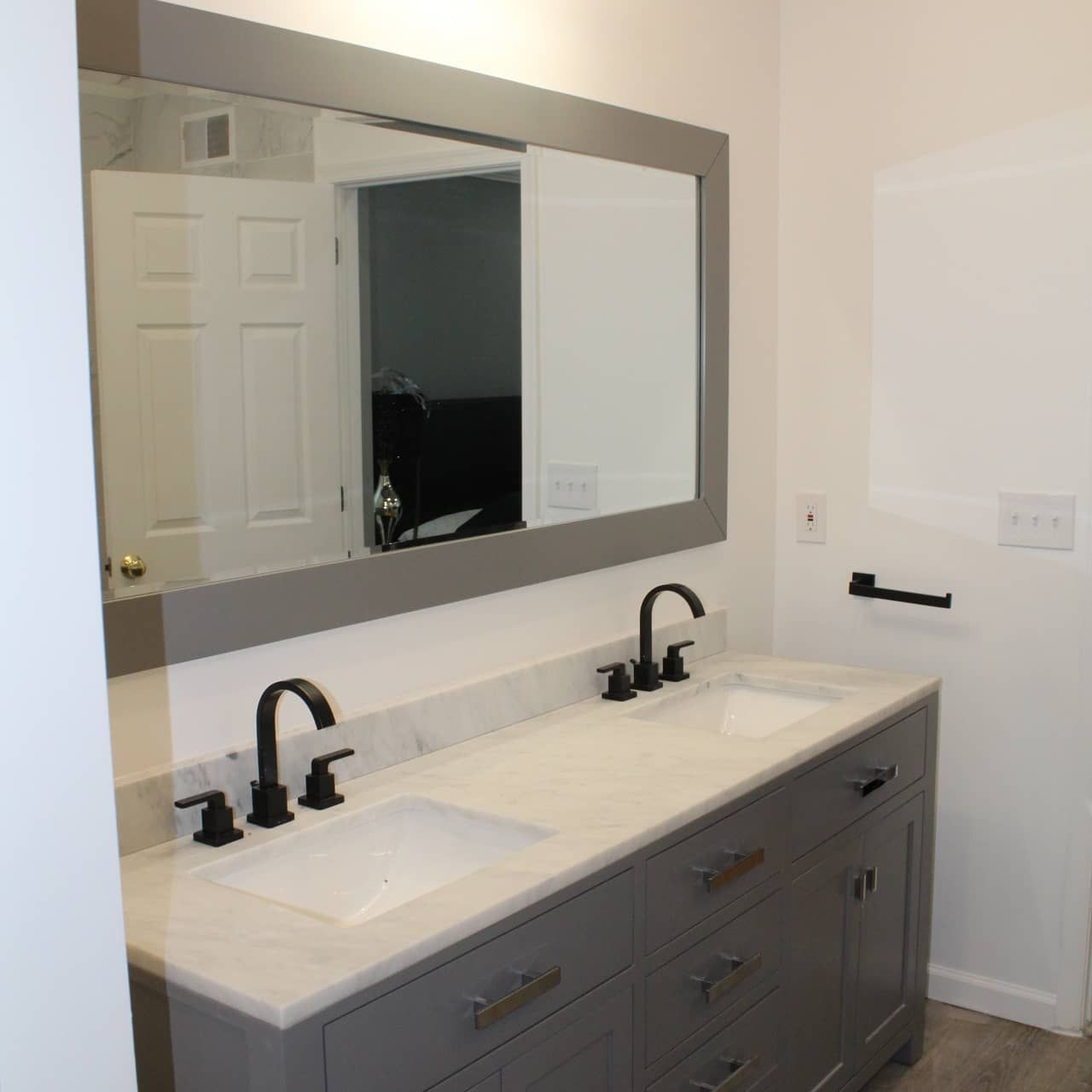 Gray bathroom vanity with two sinks, black faucets, and large mirror.