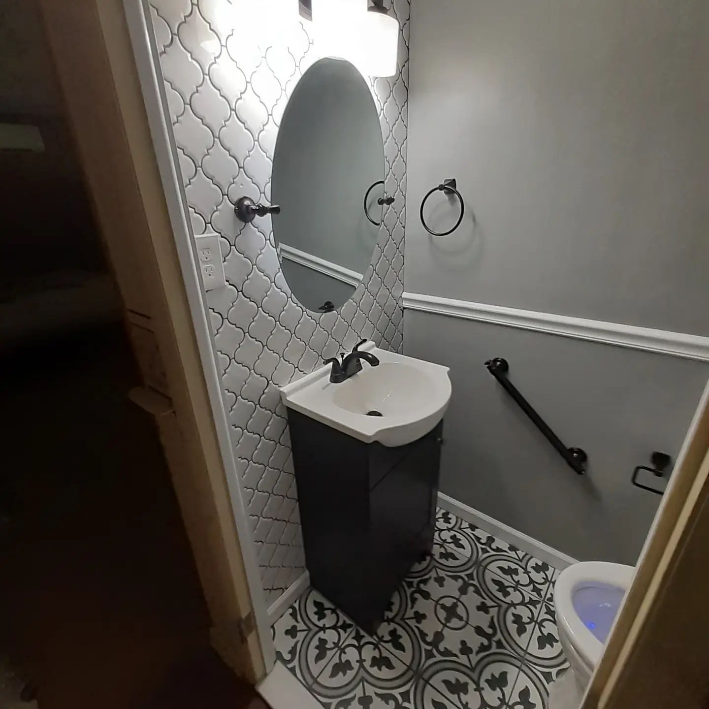 Small bathroom with pedestal sink, patterned floor, and mosaic tile backsplash.